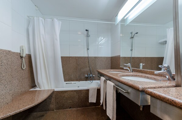 Un baño con bañera, dos lavamanos, ducha y teléfono.