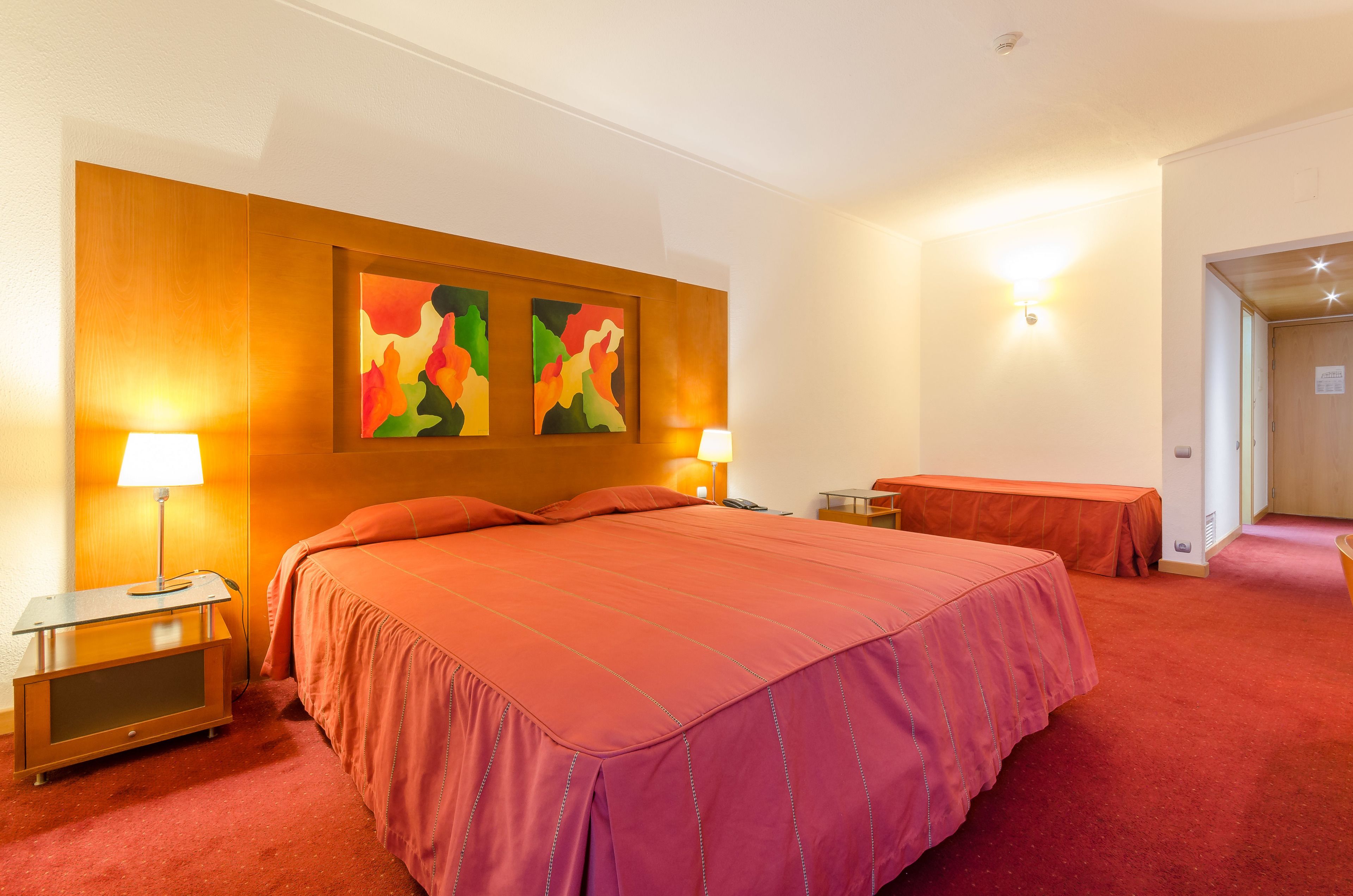 Camera d'albergo con un letto grande, due comodini con lampade, una panca e un'opera d'arte astratta appesa al muro.