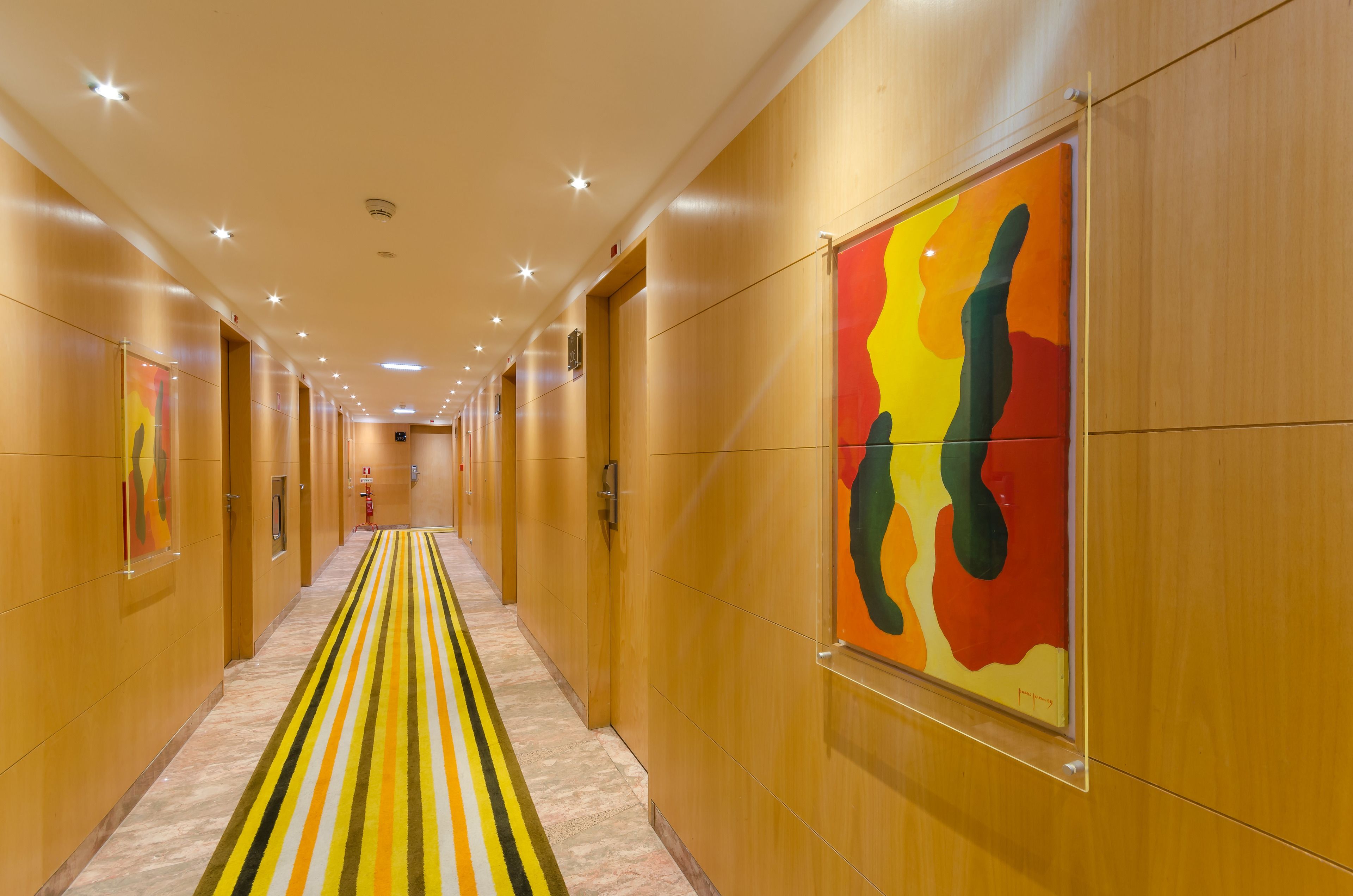 Un pasillo de hotel con alfombra a rayas, paredes de madera y un cuadro abstracto colorido.