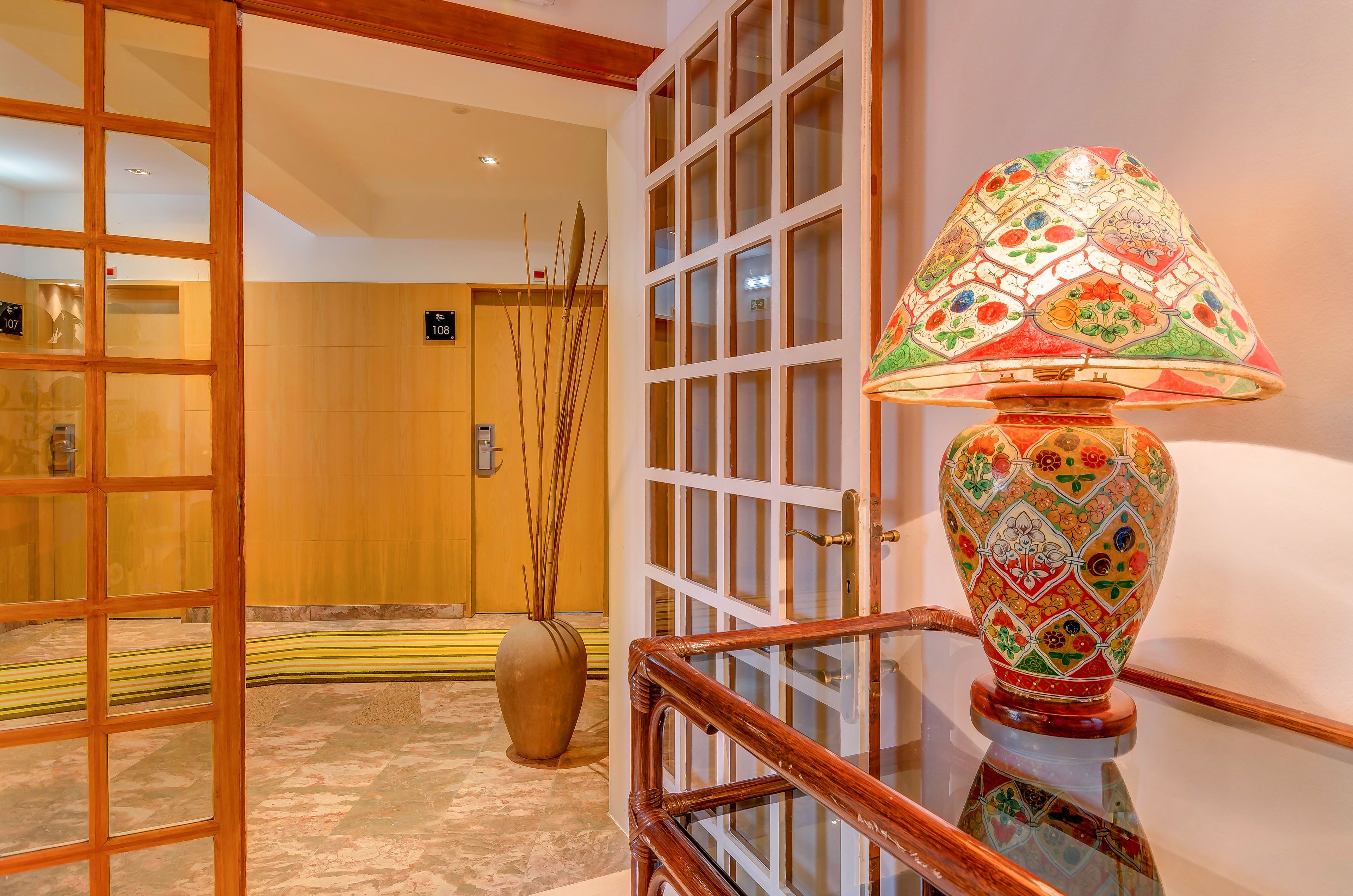 A hotel lobby with a wooden door, a glass railing, and a decorative lamp.