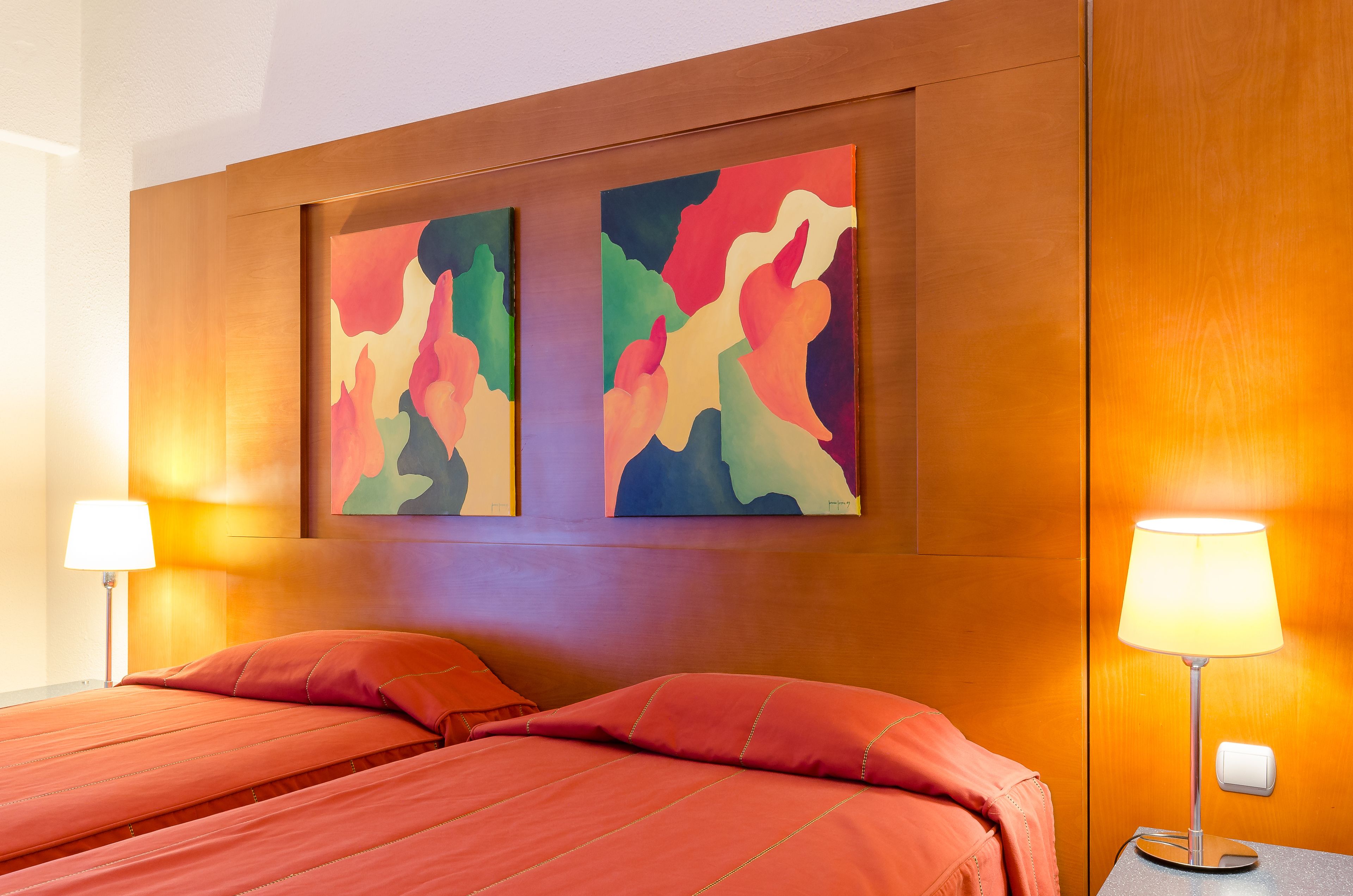A hotel room with a large bed, two wall-mounted paintings, and two bedside lamps.