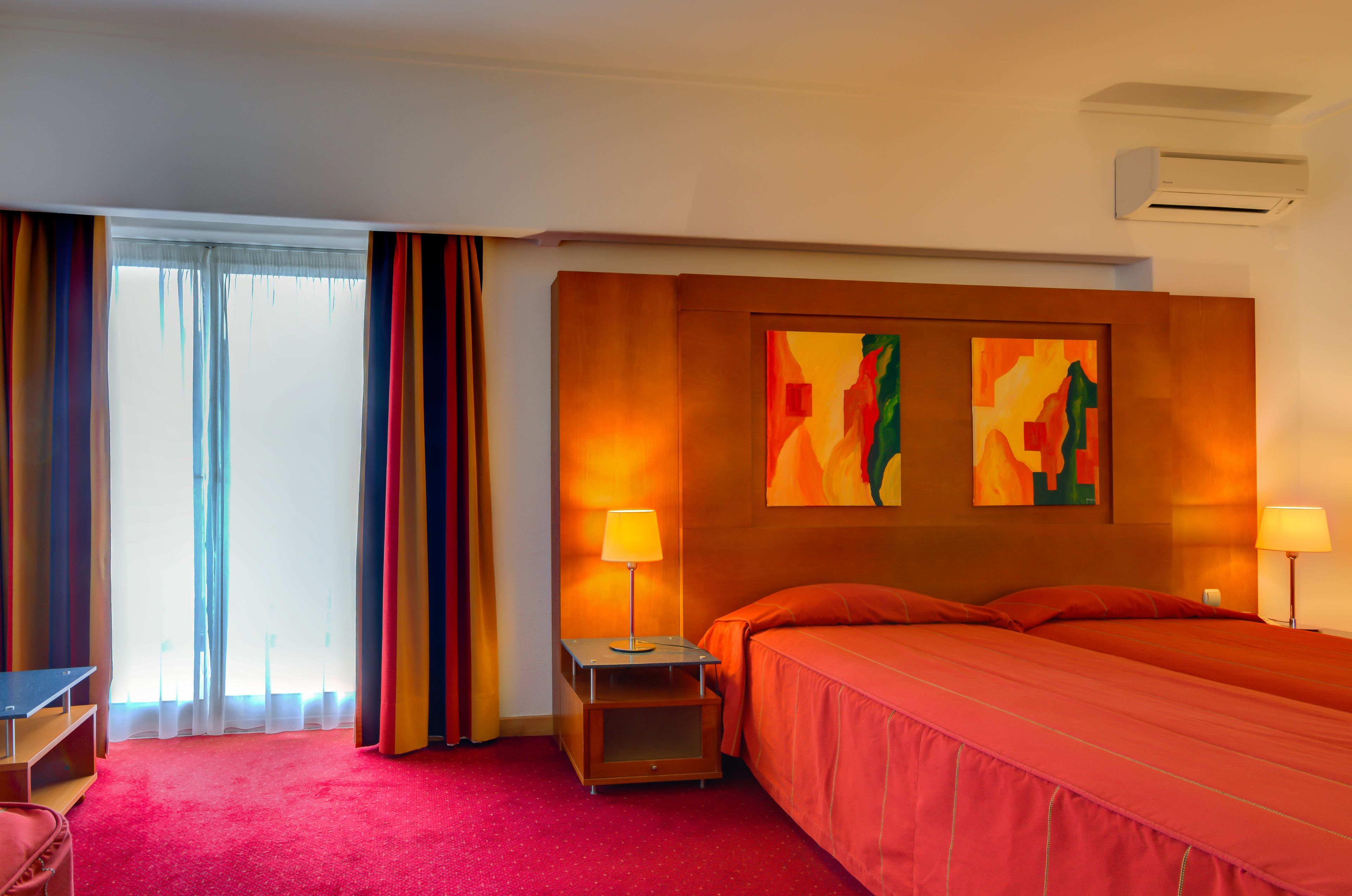 A hotel room with a bed, a nightstand with a lamp, a desk, and a chair.