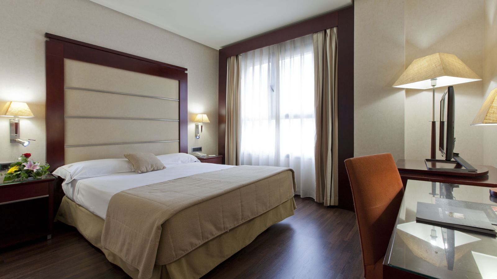 Una camera d'albergo con un letto grande, comodini, una scrivania con una sedia e una finestra con tende.