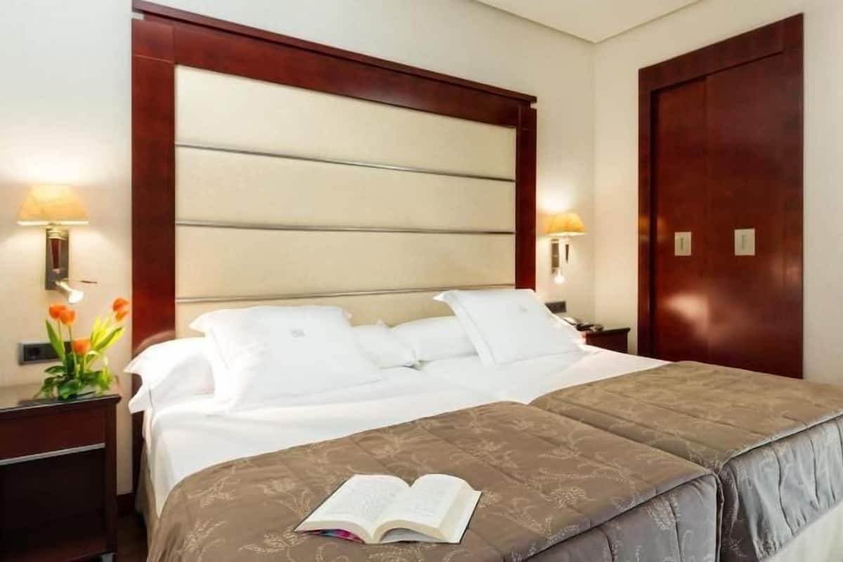 Ein Hotelzimmer mit einem großen Bett, zwei Nachttischen, einem Sessel und einem gerahmten Bild an der Wand.