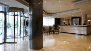 A hotel lobby with a revolving door, a reception desk, and a seating area with chairs.