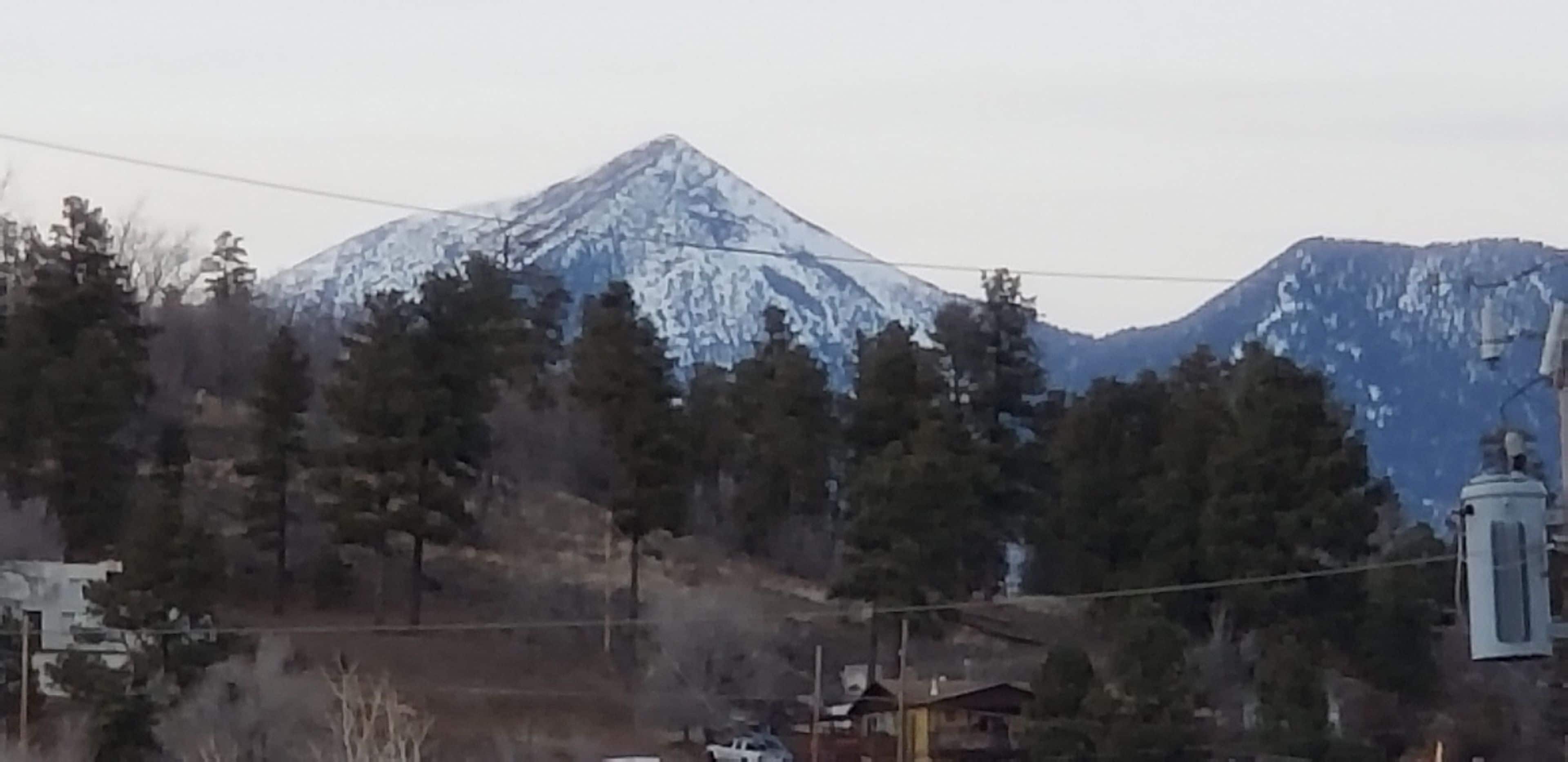 A snow-covered mountain with a few buildings and trees in the foreground.
