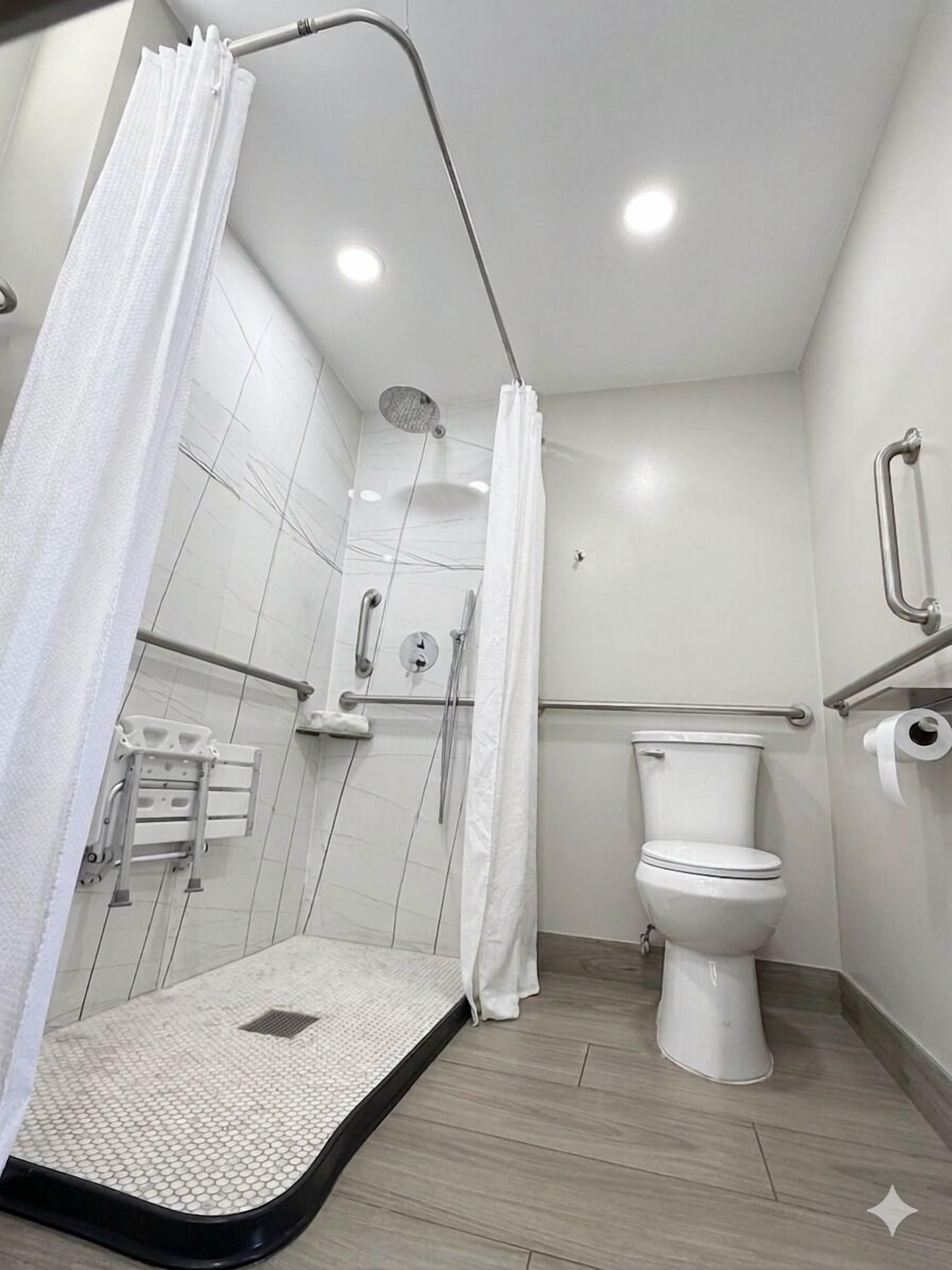 Un baño moderno con ducha, inodoro y barras de apoyo.