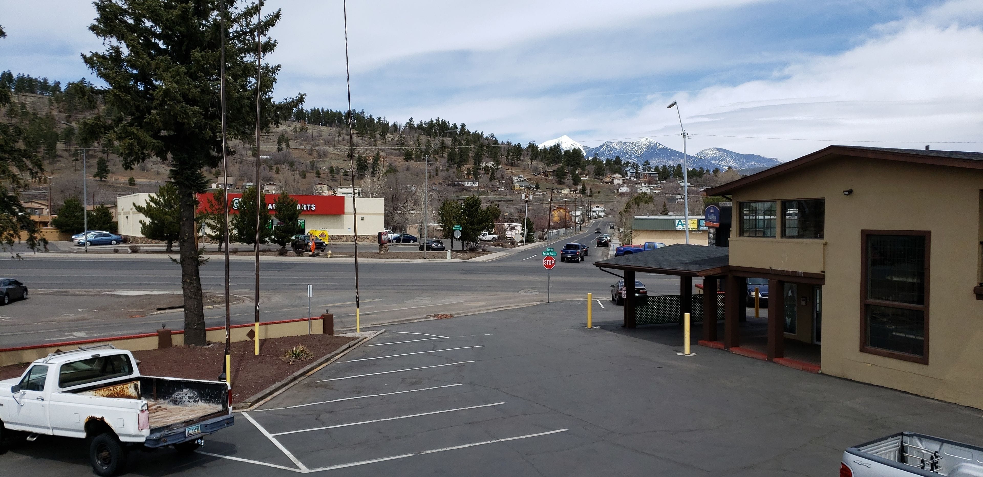 A parking lot with a white pickup truck, a building with a red sign, and a mountain in the background.
