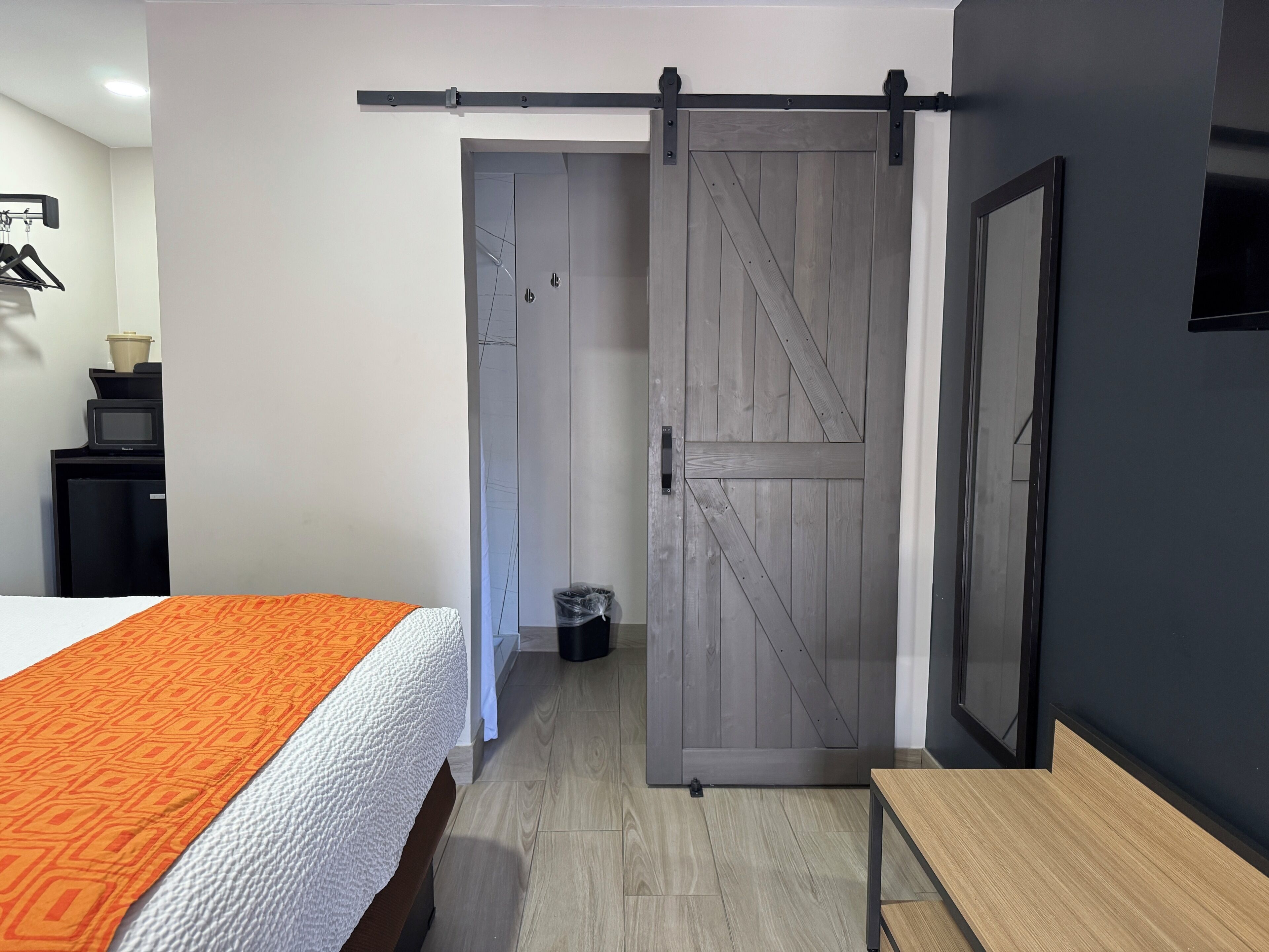 Una habitación con una cama, una puerta corredera de madera, una mesita pequeña y un televisor montado en la pared.