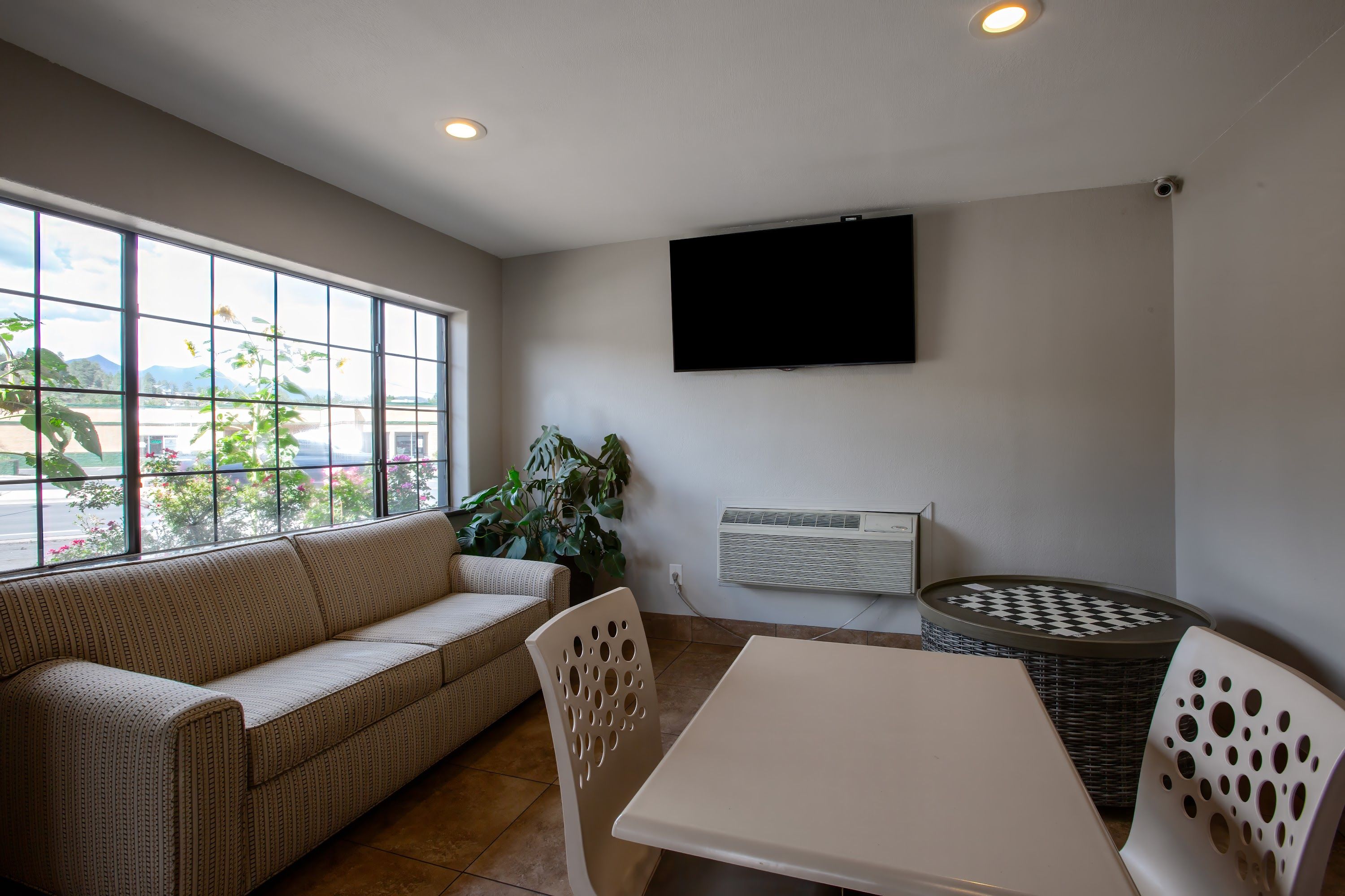 A room with a sofa, a table, chairs, a television, and a window with a view.