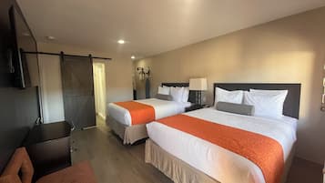 A hotel room with two beds, a desk, a chair, and a TV.