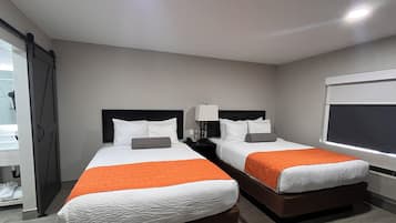 A hotel room with two beds, a nightstand with a lamp, a window with blinds, and a door with a curtain.