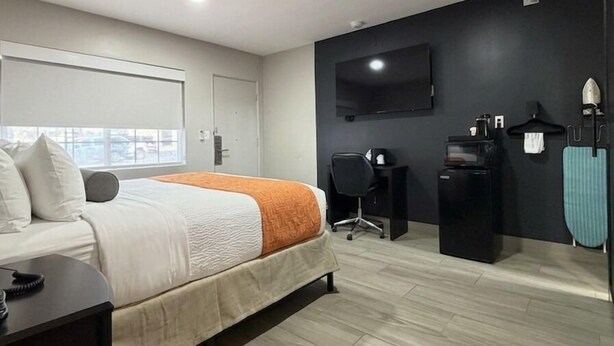 A modern hotel room with a bed, a desk, a chair, a TV, and a coffee machine.