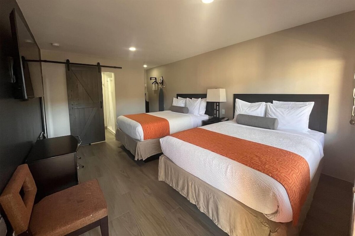 A hotel room with two beds, a desk, and a chair.