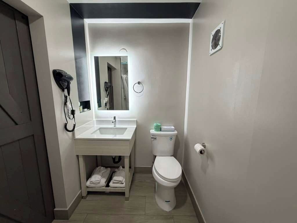 A compact bathroom with a sink, mirror, toilet, and towel rack.