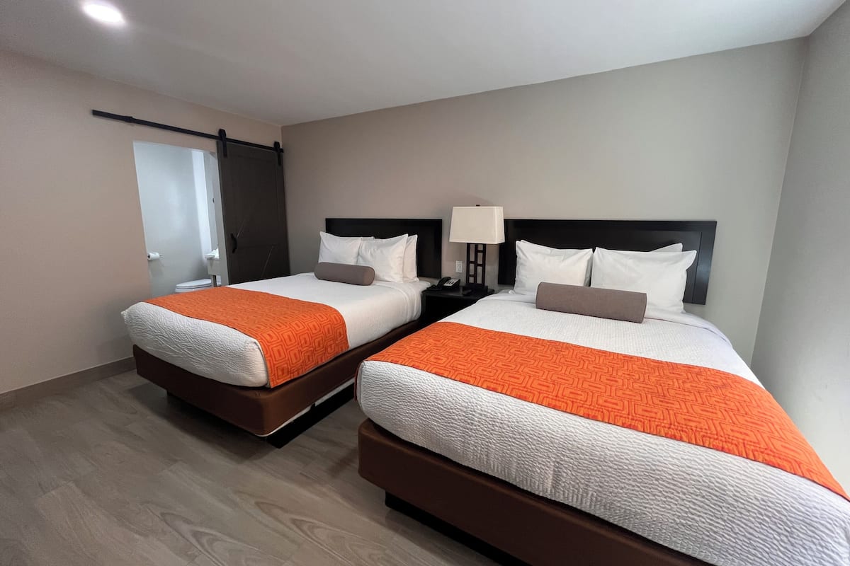 Ett hotellrum med två sängar, var och en med ett orange- och vitrandigt sängöverkast, ett nattduksbord med en lampa och en dörr med en handduksställning.