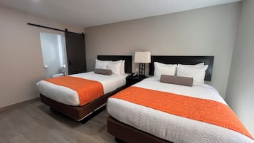 A hotel room with two beds, each with an orange and white bedspread, a nightstand with a lamp, and a door with a towel rack.
