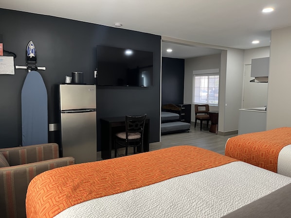 A hotel room with two beds, a desk, a chair, a small kitchenette, and a window.