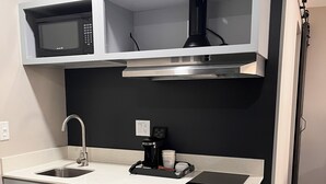 A modern kitchen with grey cabinets, a stainless steel sink, a microwave, and a coffee maker.