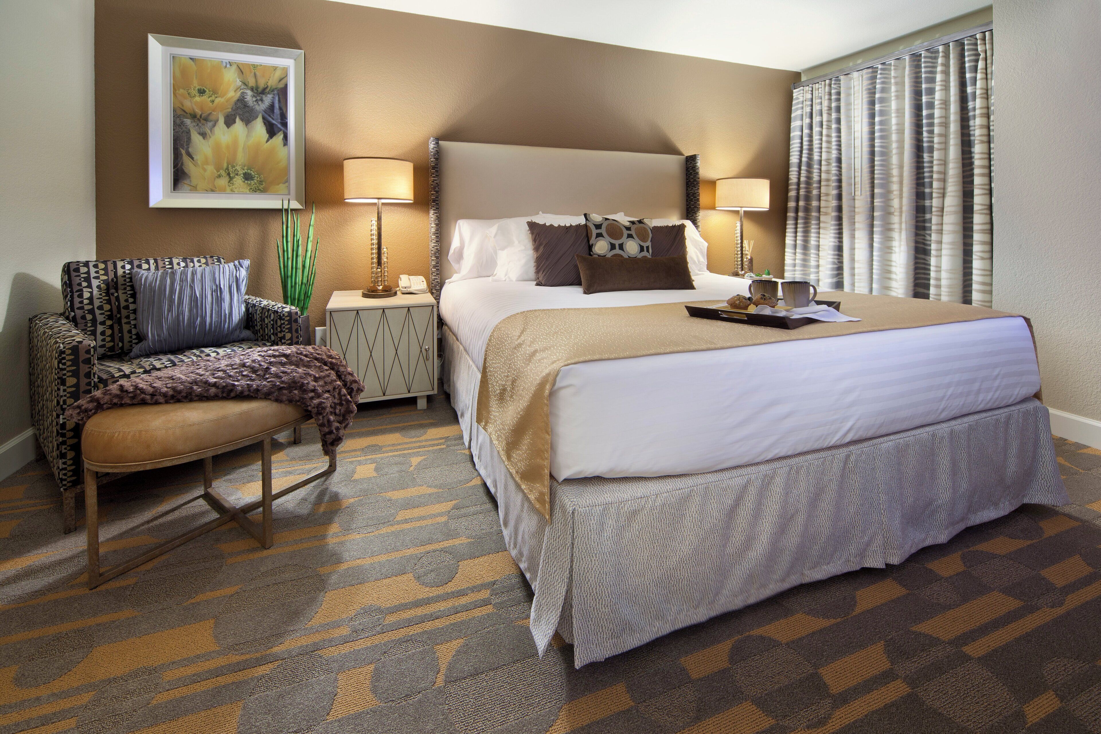 A hotel room with a bed, a chair, a nightstand, and a lamp.