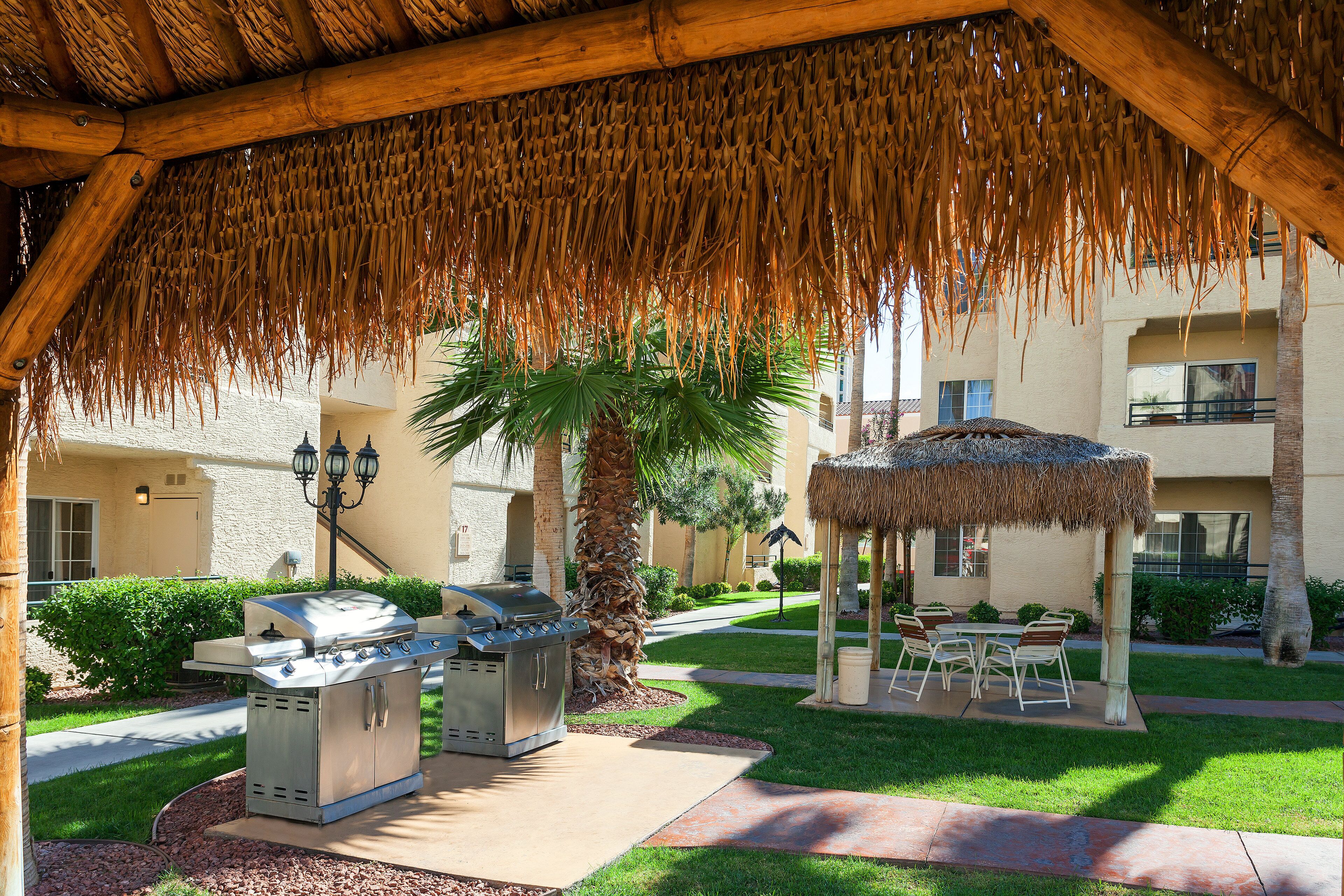 Un patio exterior con una parrilla, mobiliario y un pabellón con techo de paja.