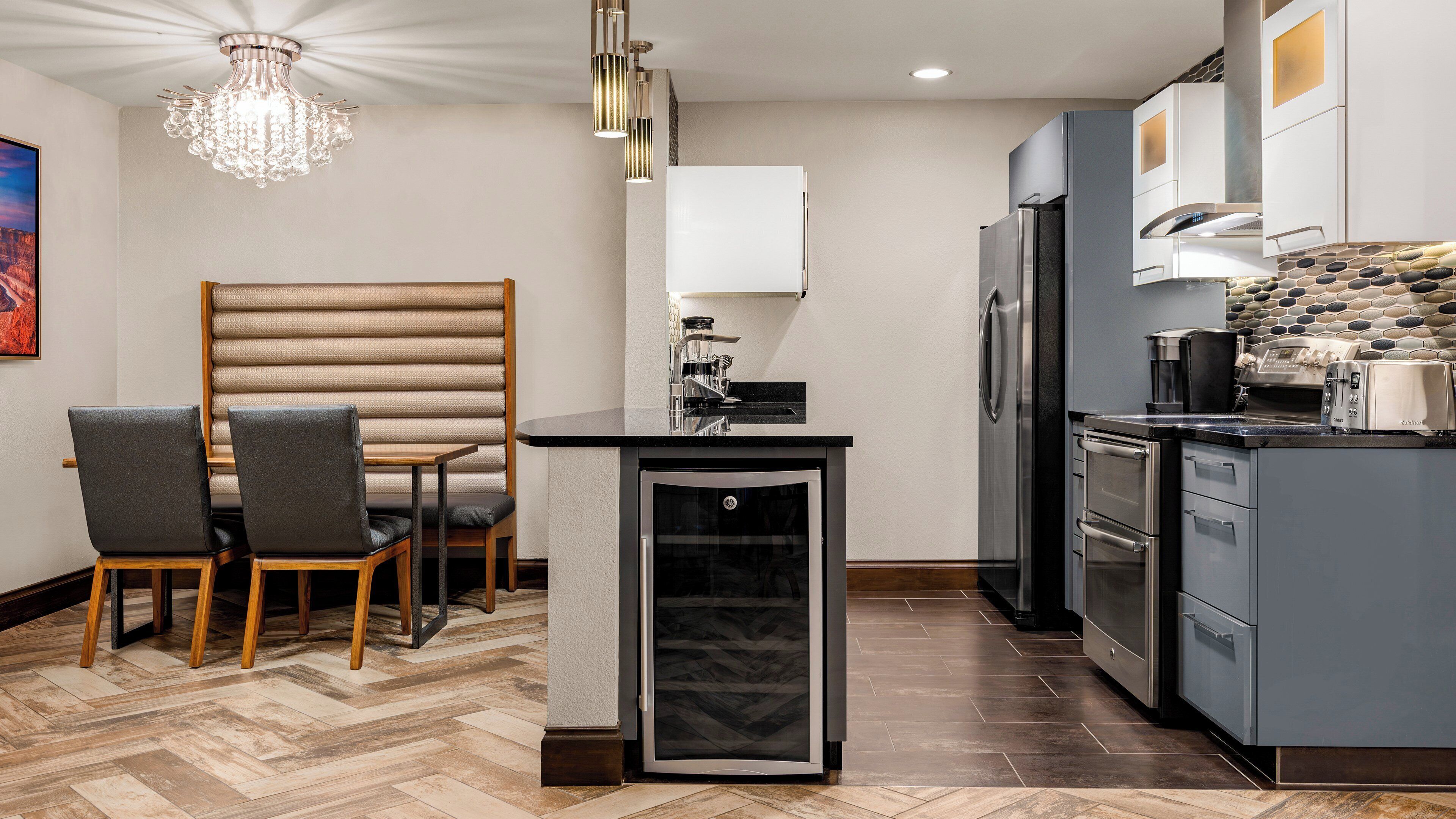 A modern kitchen with a built-in refrigerator, oven, and coffee maker. There is a small island with a sink and a chandelier above.