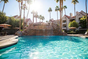A swimming pool with a rock feature, surrounded by palm trees and hotel buildings. - Holiday Inn Club Vacations at Desert Club Resort by IHG (Las Vegas)