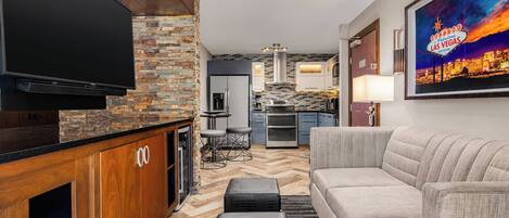Uma sala de estar moderna com televisão de tela plana, parede de destaque em pedra, cozinha ao fundo e um letreiro emoldurado de Las Vegas.