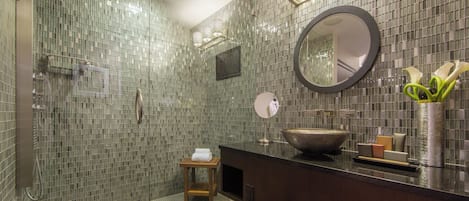 A modern bathroom with a glass shower enclosure, a round mirror, a large sink, and a small wooden stool.
