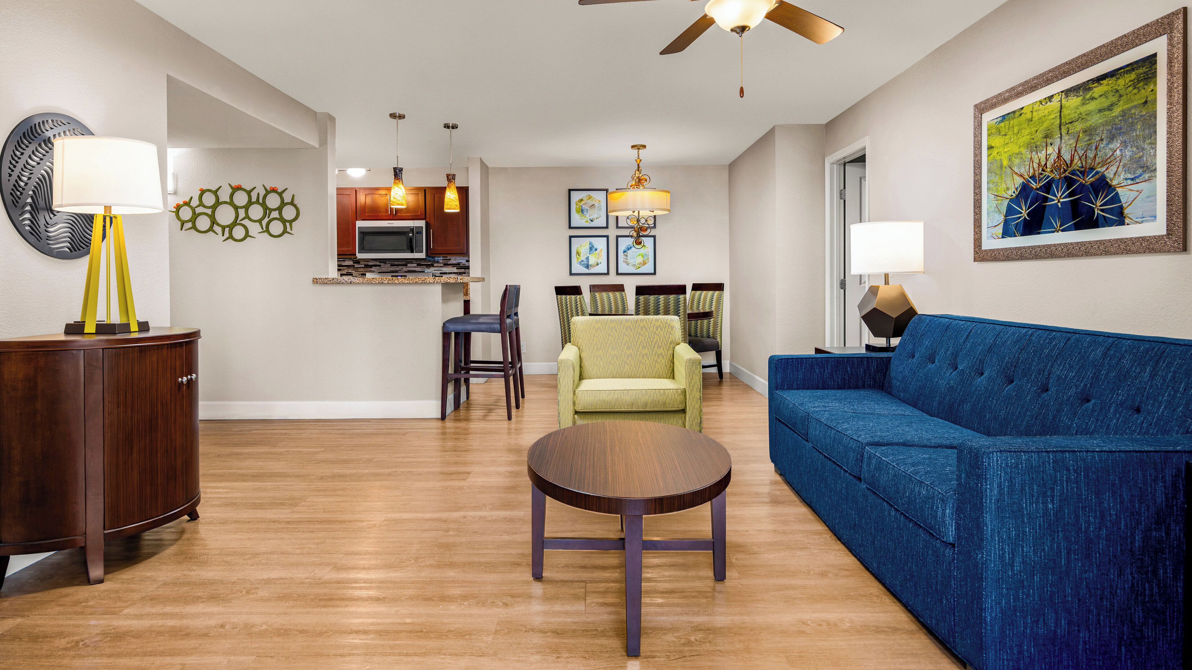 Una sala de estar moderna con un sofá azul, una mesa de centro de madera y un comedor con sillas, y una cocina al fondo.