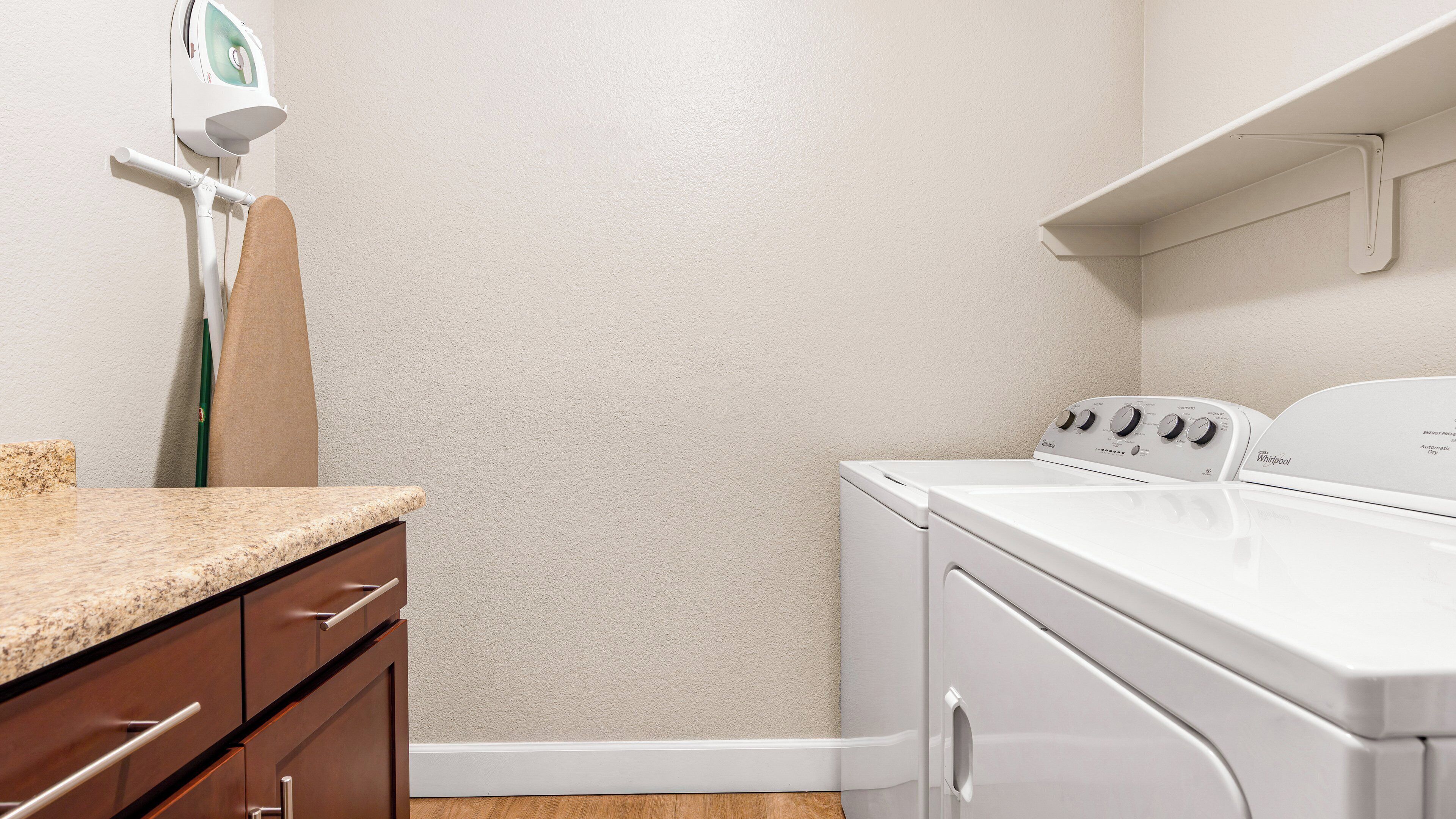 Une buanderie équipée d’un lave-linge, d’un sèche-linge et d’une planche à repasser fixée au mur.