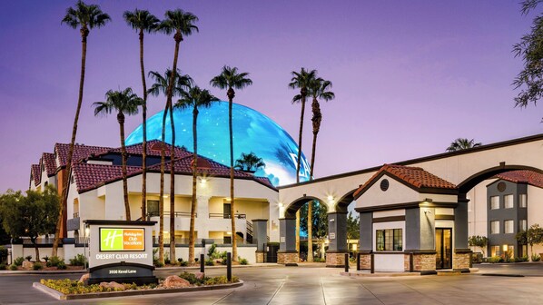 A Holiday Inn with a large dome structure, palm trees, and a sign indicating it's a Desert Club Resort. - Holiday Inn Club Vacations at Desert Club Resort by IHG (Las Vegas)