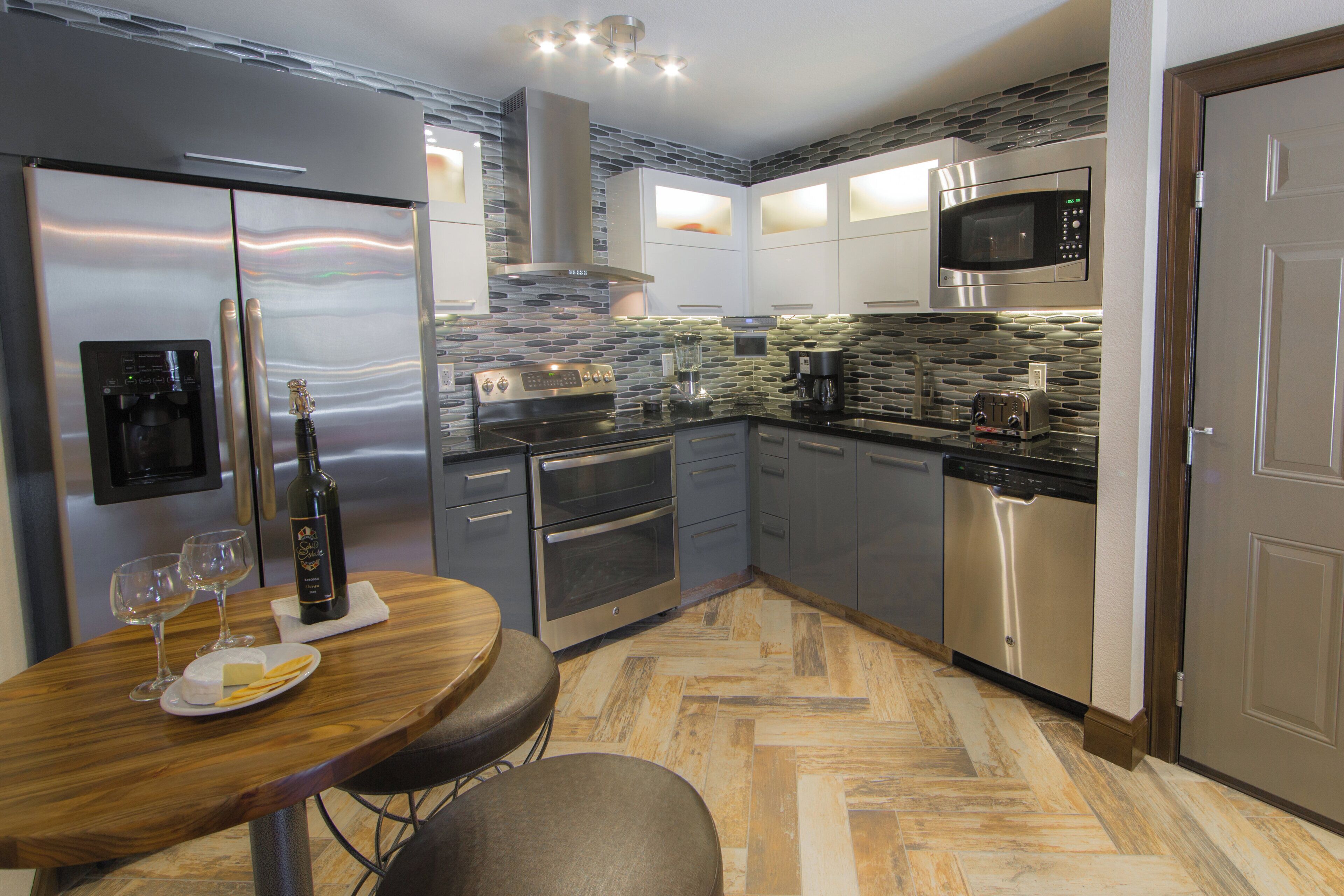 A modern kitchen with stainless steel appliances, a stone backsplash, and a herringbone wood floor.