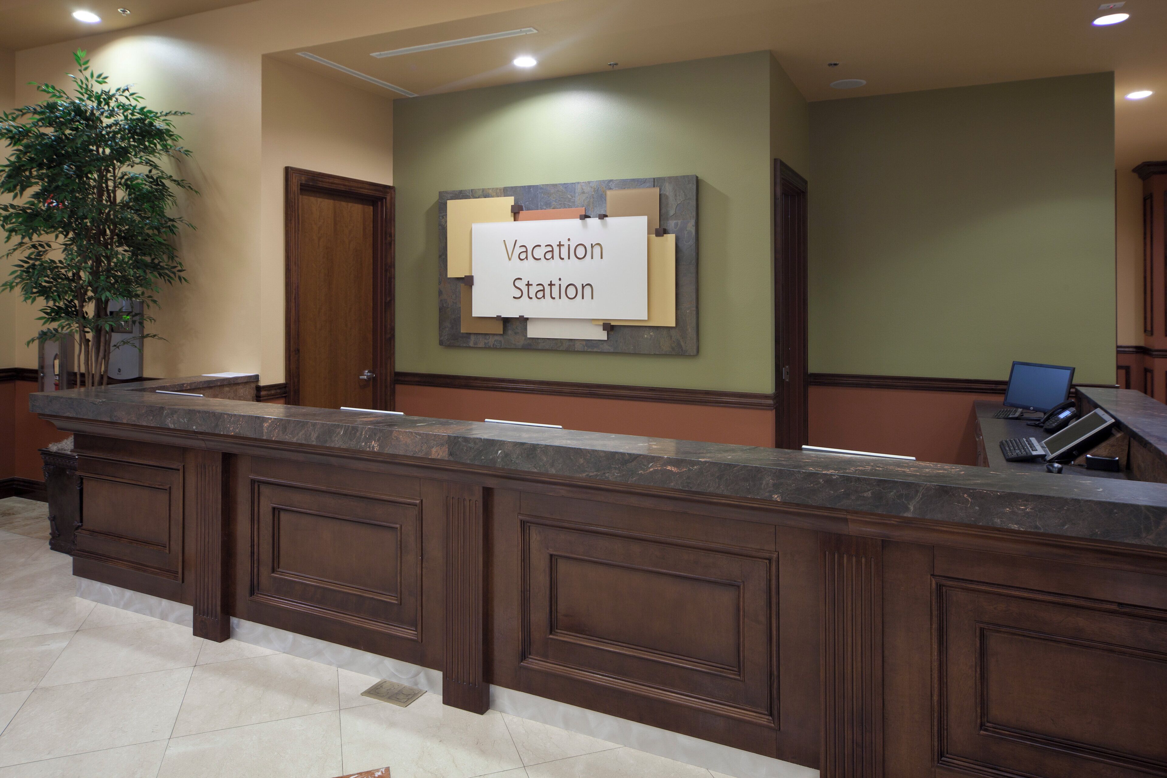 Un mostrador de recepción con un cartel que dice 'Vacation Station' y una planta en maceta a la izquierda.