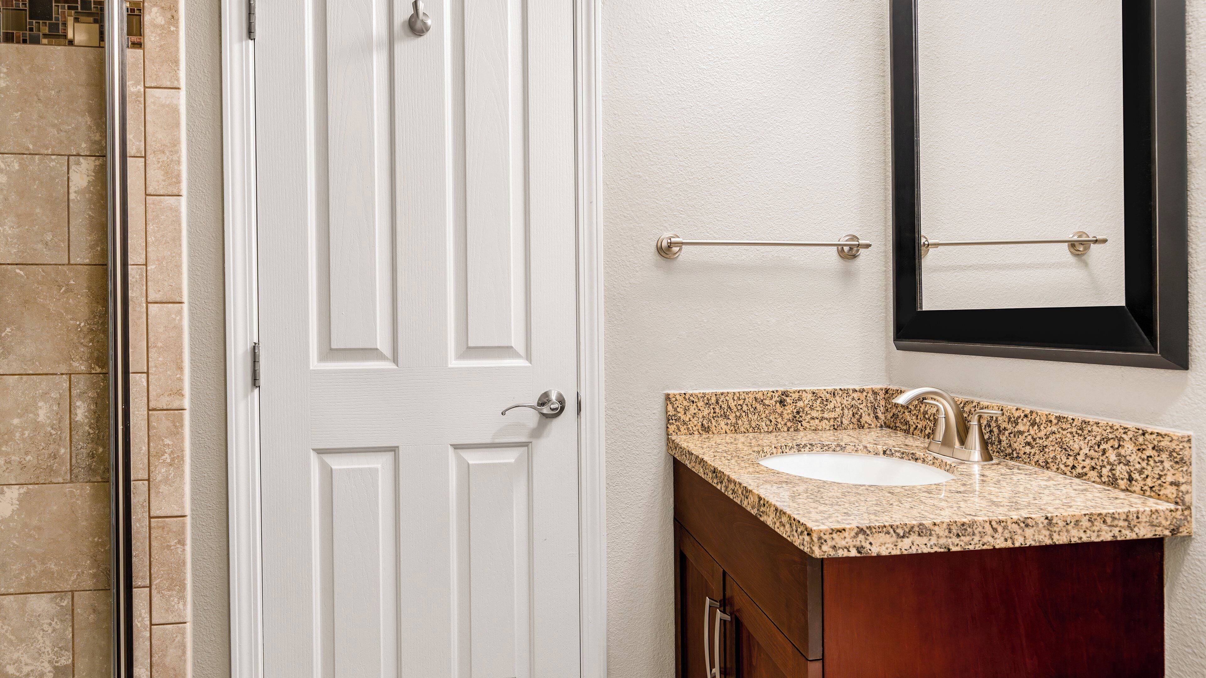 A bathroom with a white door, a granite countertop sink, and a wooden vanity.