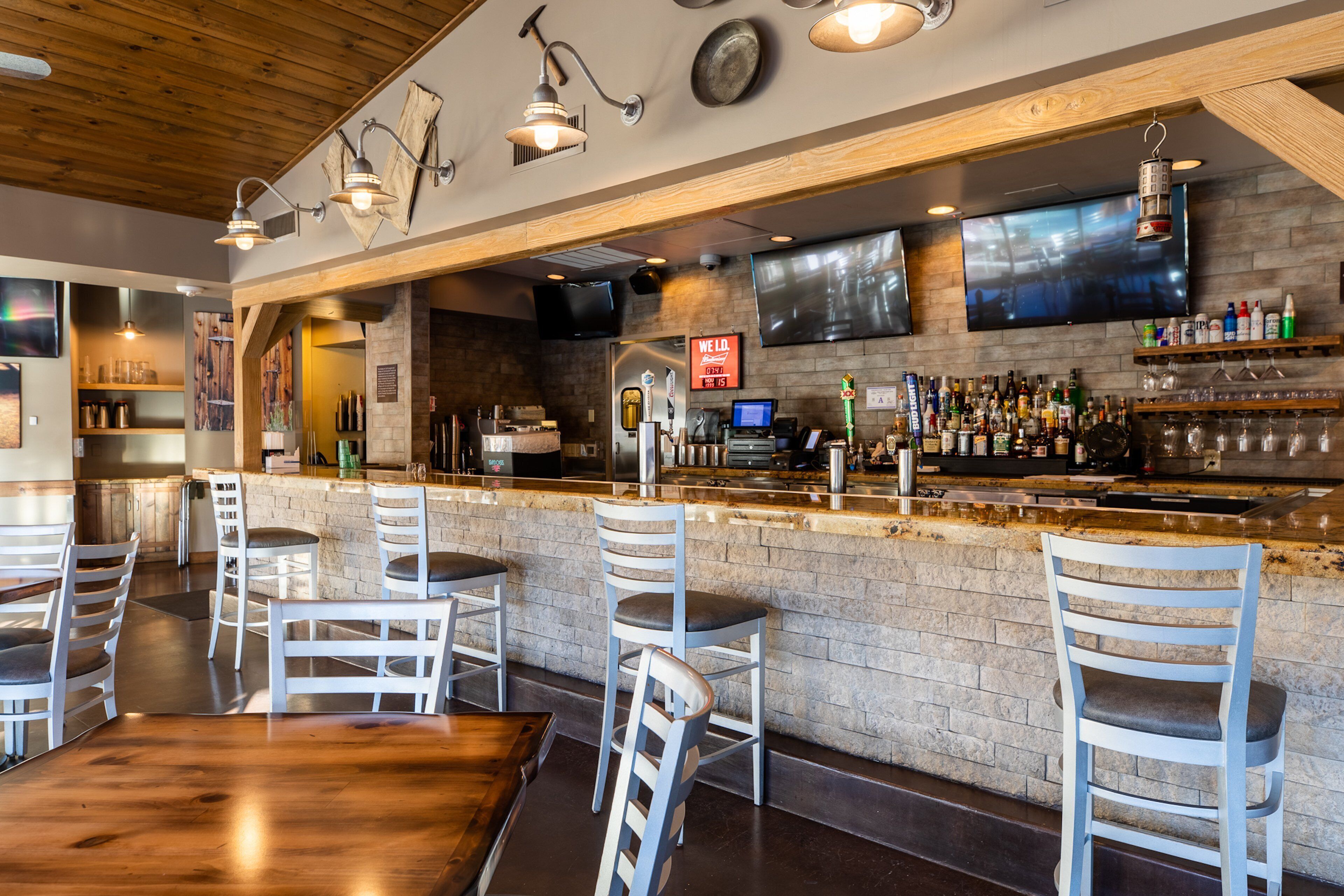 A bar area with a brick counter, white bar stools, and a television mounted on the wall.