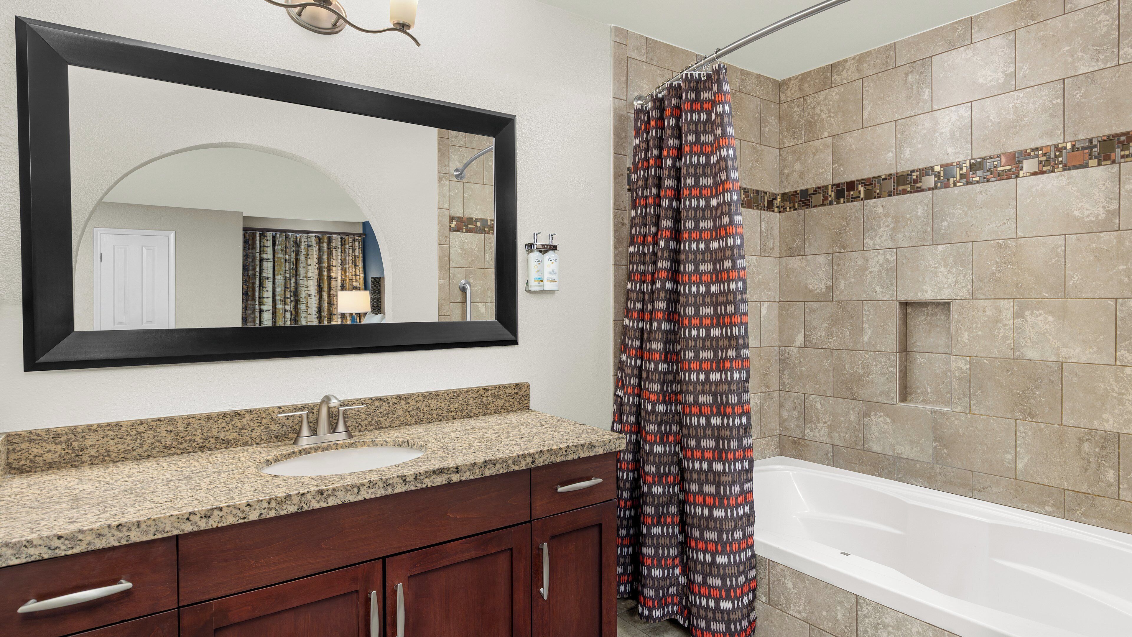 Une salle de bain avec un grand miroir, un lavabo, un meuble-vasque avec des tiroirs, un rideau de douche et une baignoire.
