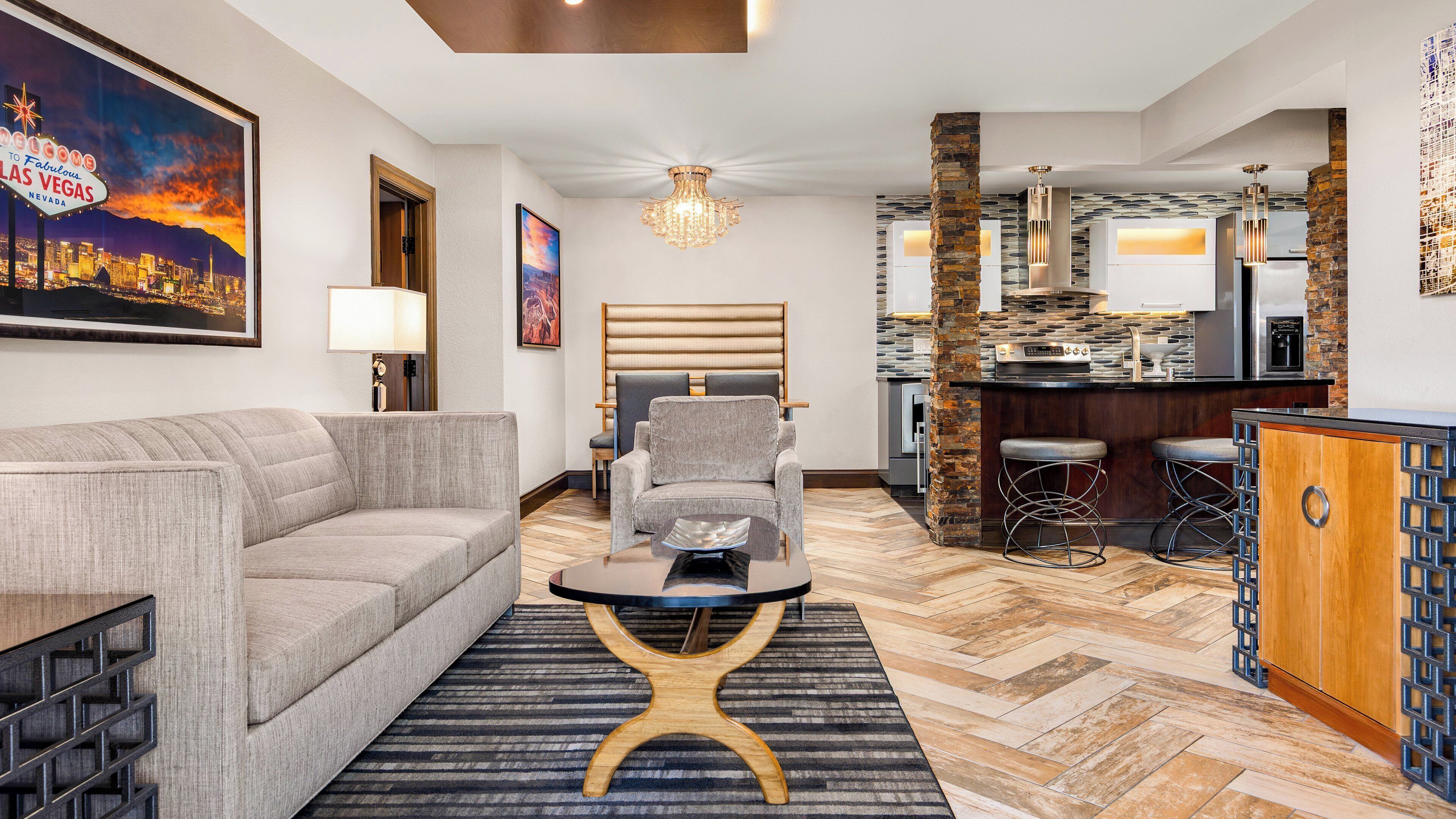 Un salon moderne avec un canapé, un fauteuil et une table basse. Il y a également un coin cuisine avec un bar et des tabourets.