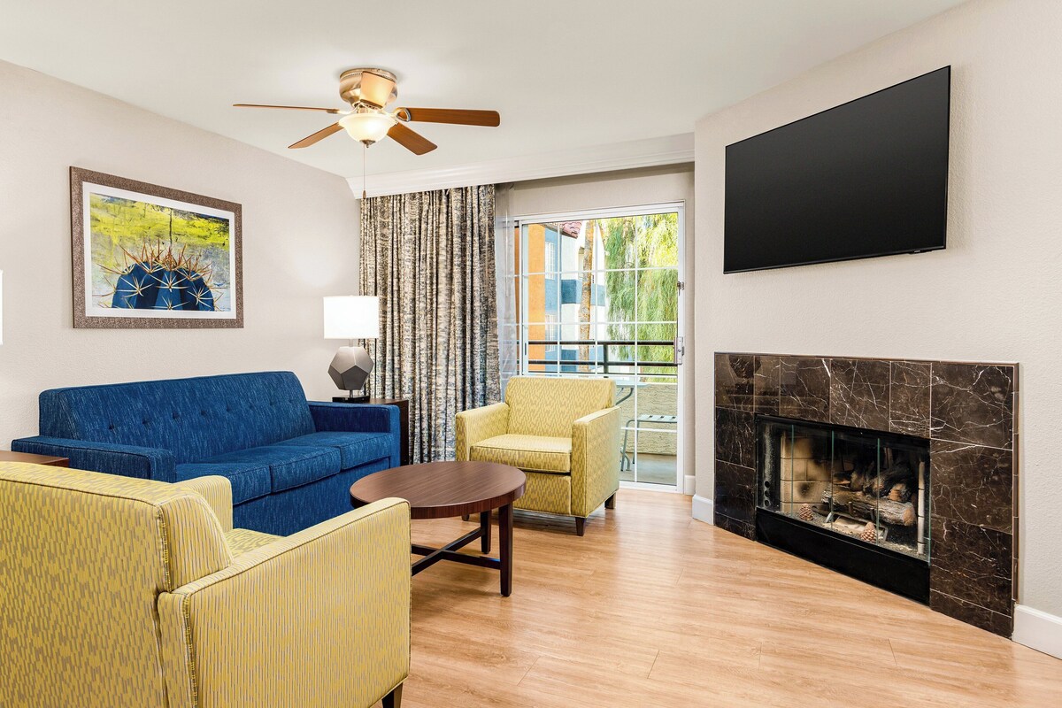 A living room with a blue sofa, yellow armchairs, a fireplace, and a ceiling fan.