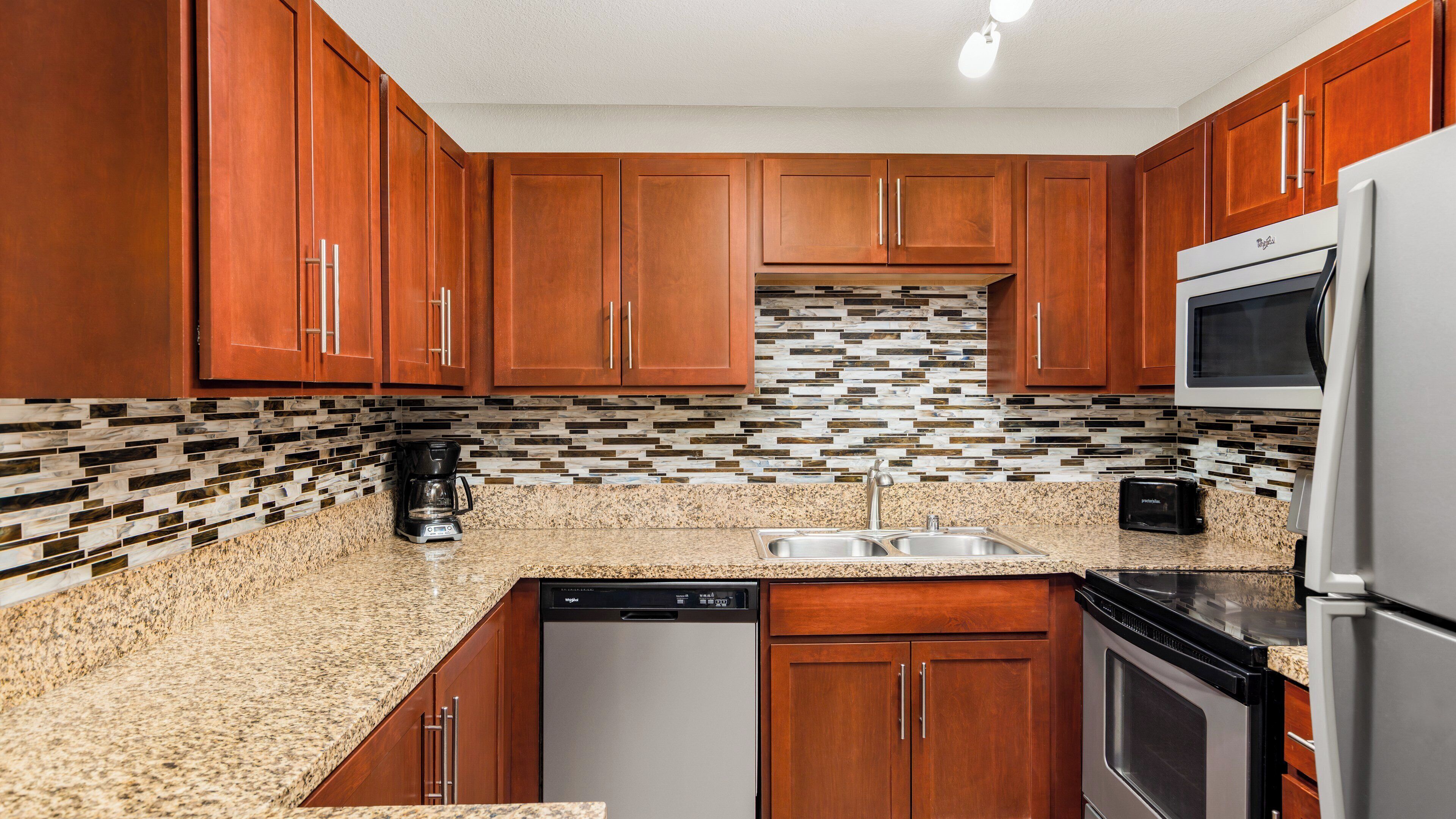 A kitchen with wooden cabinets, a granite countertop, a dishwasher, a microwave, and a tiled backsplash.
