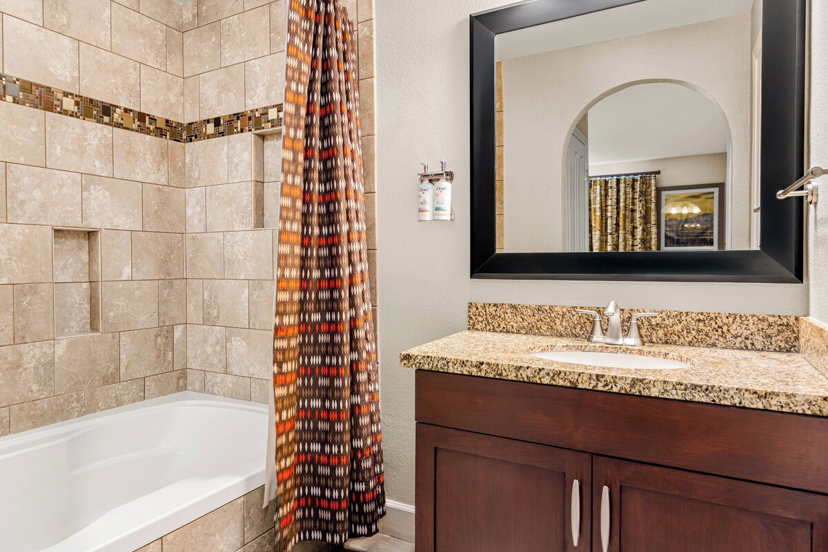 A bathroom with a shower, a sink with a granite countertop, and a mirror above the sink.