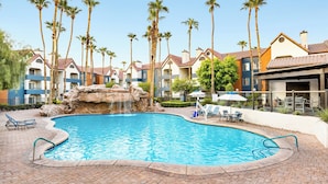 A swimming pool with a waterfall feature, surrounded by palm trees and a poolside area with lounge chairs and umbrellas. - Holiday Inn Club Vacations at Desert Club Resort by IHG (Las Vegas)