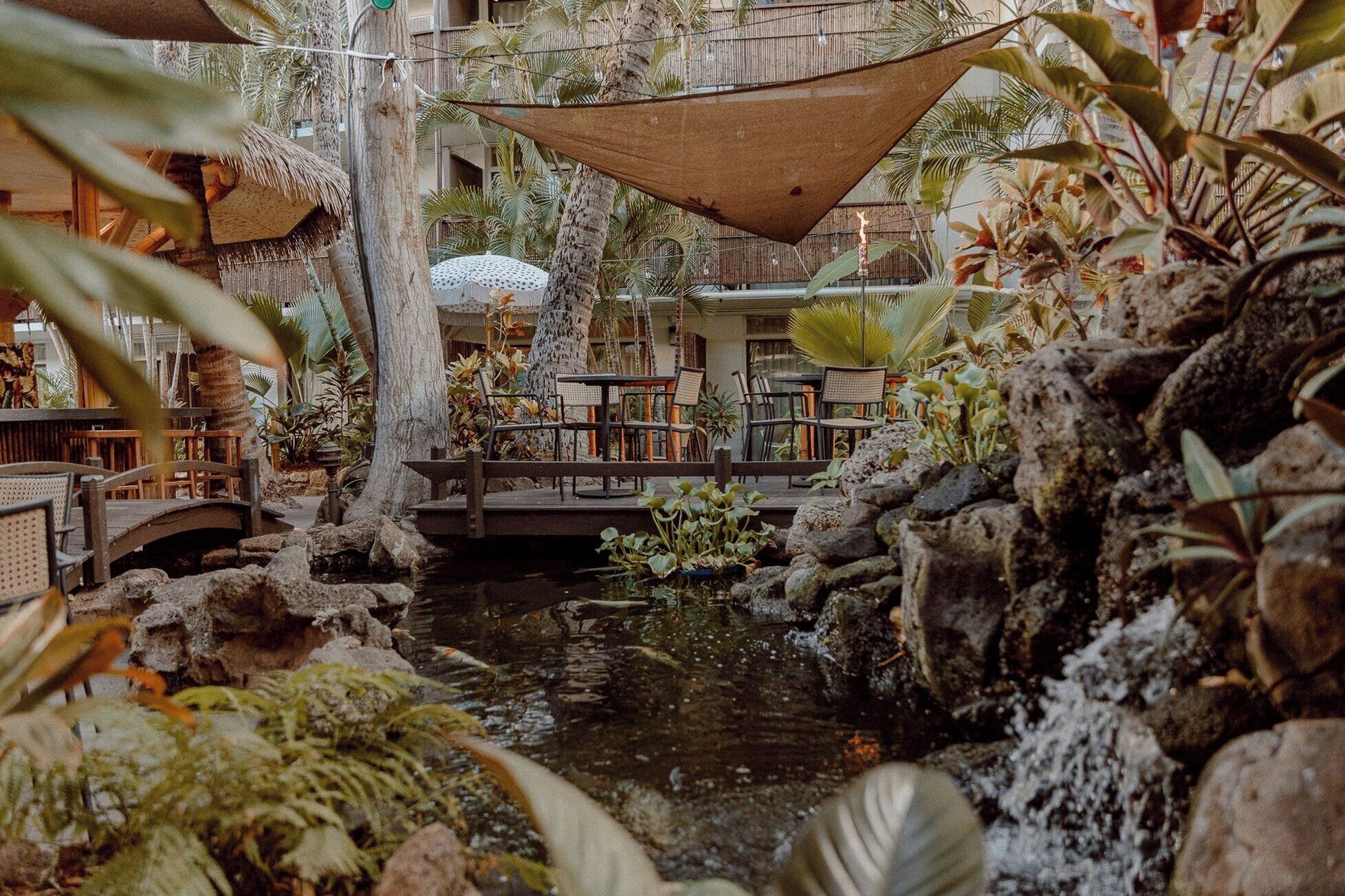 An indoor garden with a water feature, seating area, and tropical plants.