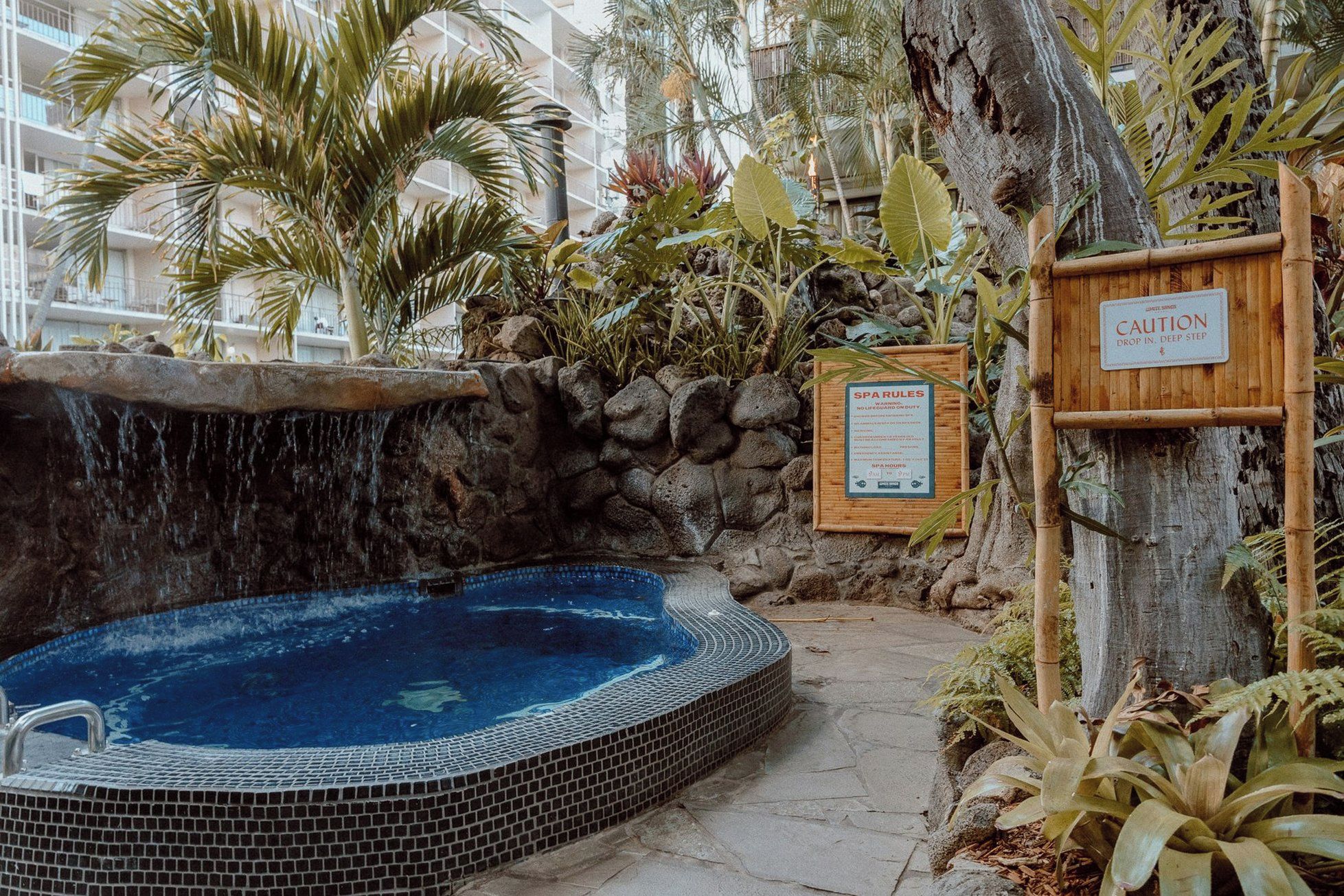 Zona de spa con un jacuzzi, un cartel de madera con normas del spa y una cascada.