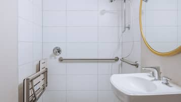 A bathroom with white tiles, a sink, a mirror, and a shower with a grab bar.