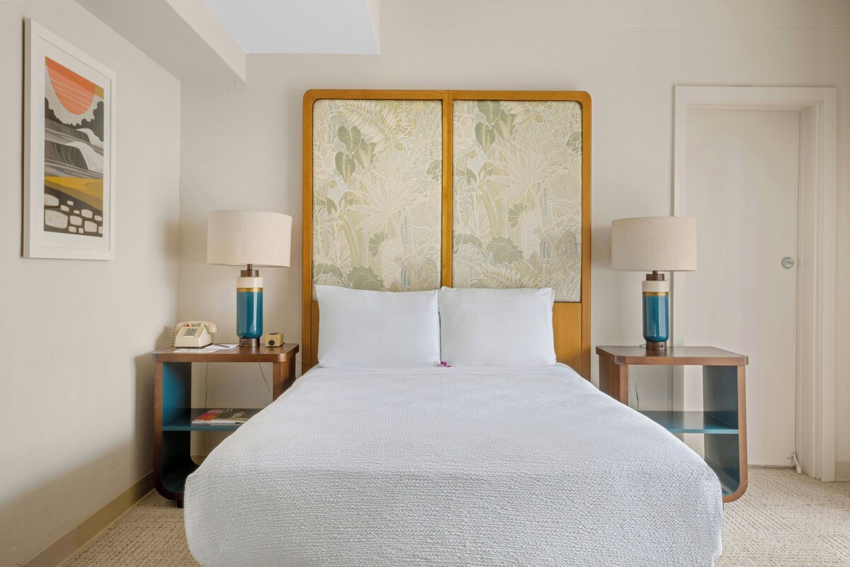 A hotel room with a large bed, two bedside tables with lamps, a telephone, and a framed picture on the wall.