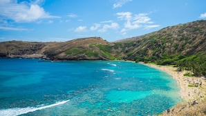 Paisaje costero con una playa, aguas turquesas cristalinas y colinas al fondo.