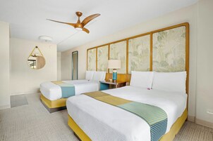 Ein Hotelzimmer mit zwei Betten, einem Deckenventilator, einem Nachttisch mit Lampe, einem Spiegel und einer Wand mit Blumenmuster.