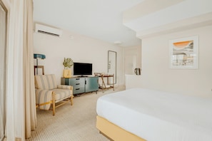 A hotel room with a bed, a TV, a desk, a chair, a plant, and a painting. - White Sands Hotel (Honolulu)