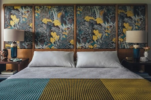 A hotel room with a large bed, two nightstands, a wall with a floral tapestry, and a lamp on each nightstand.